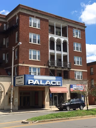 Brick four-story building with blue Palace storefront sign and awning along a street.