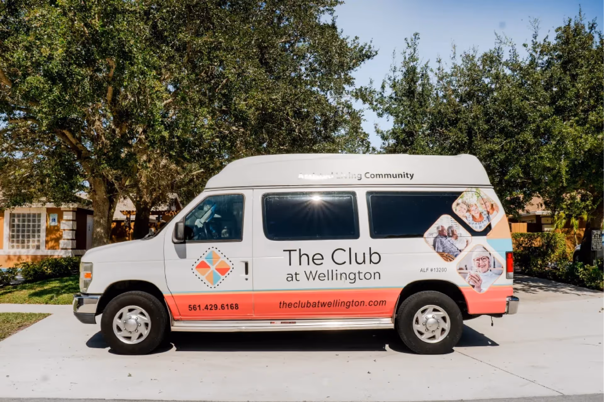 Branded shuttle van for The Club at Wellington parked on a driveway in front of trees and a building.
