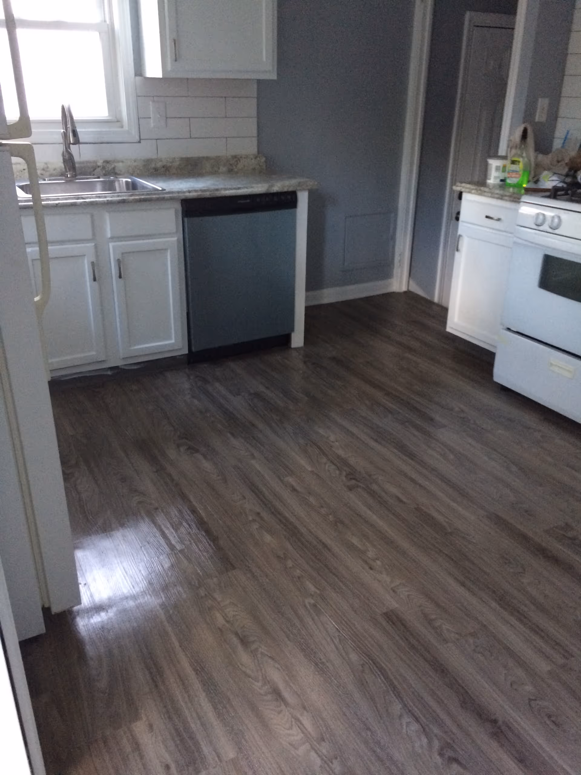 A clean residential kitchen with white cabinets, sink, dishwasher, stove, and dark wood floor
