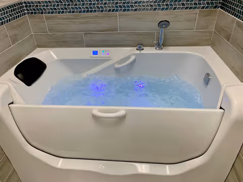 White accessible bathtub with built-in seat and blue LED jets in a tiled bathroom.
