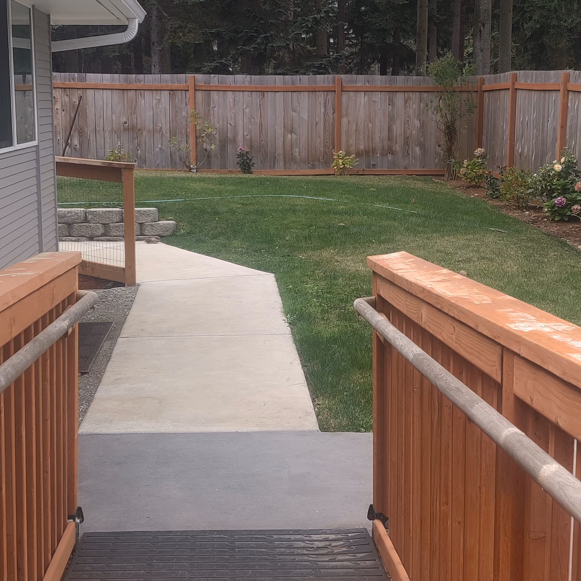 Backyard view of Sapphire Adult Family Home with wooden railing, path, lawn, and fence.