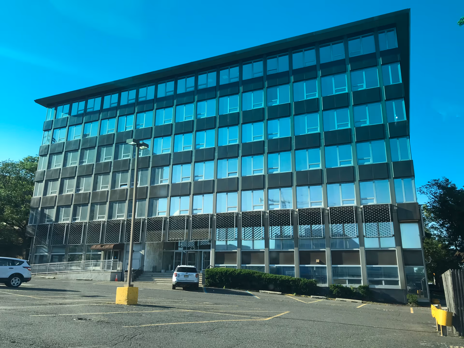 Modern, glass-front, multi-story building with a parking lot in front.