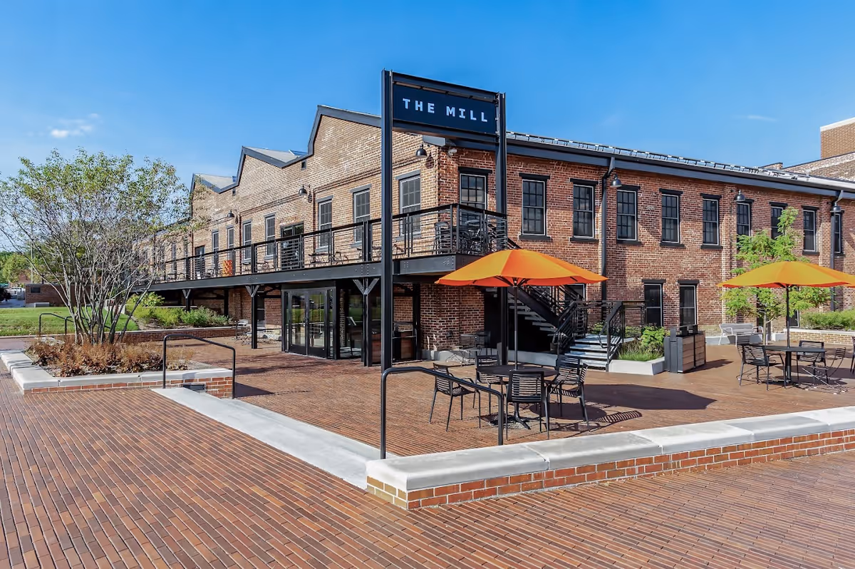 Brick senior living building with an outdoor patio, tables, chairs, and orange umbrellas.