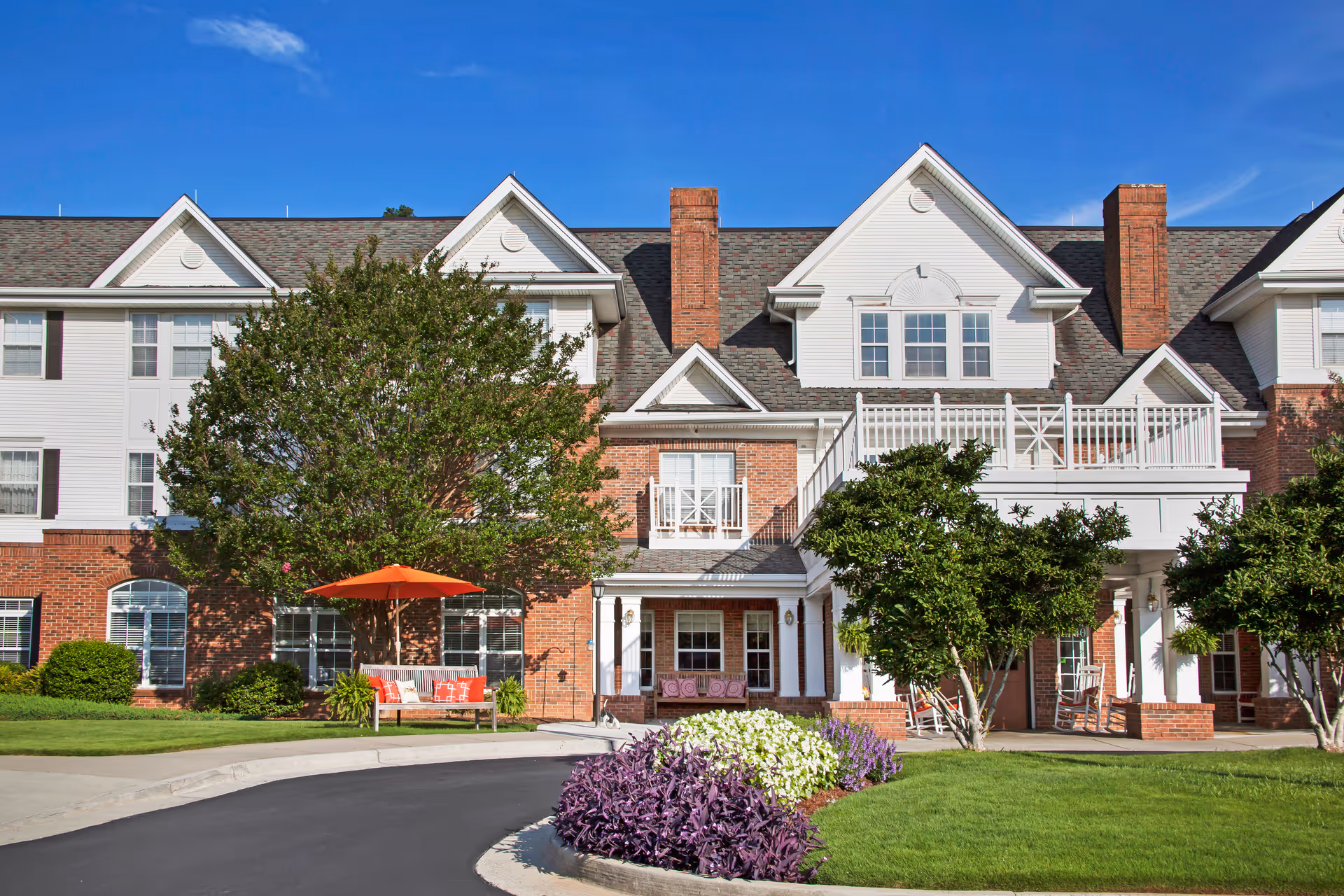Front view of Brighton Gardens of Dunwoody with brick and white facade, trees, and outdoor seating.