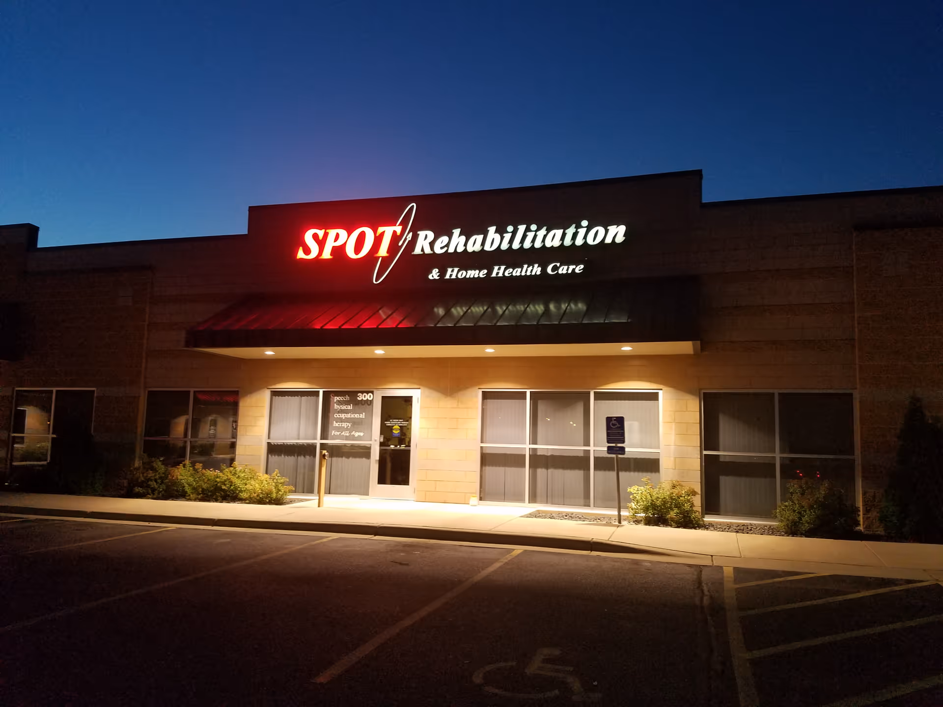 Nighttime exterior of SPOT Rehabilitation and Home Health Care building with illuminated sign