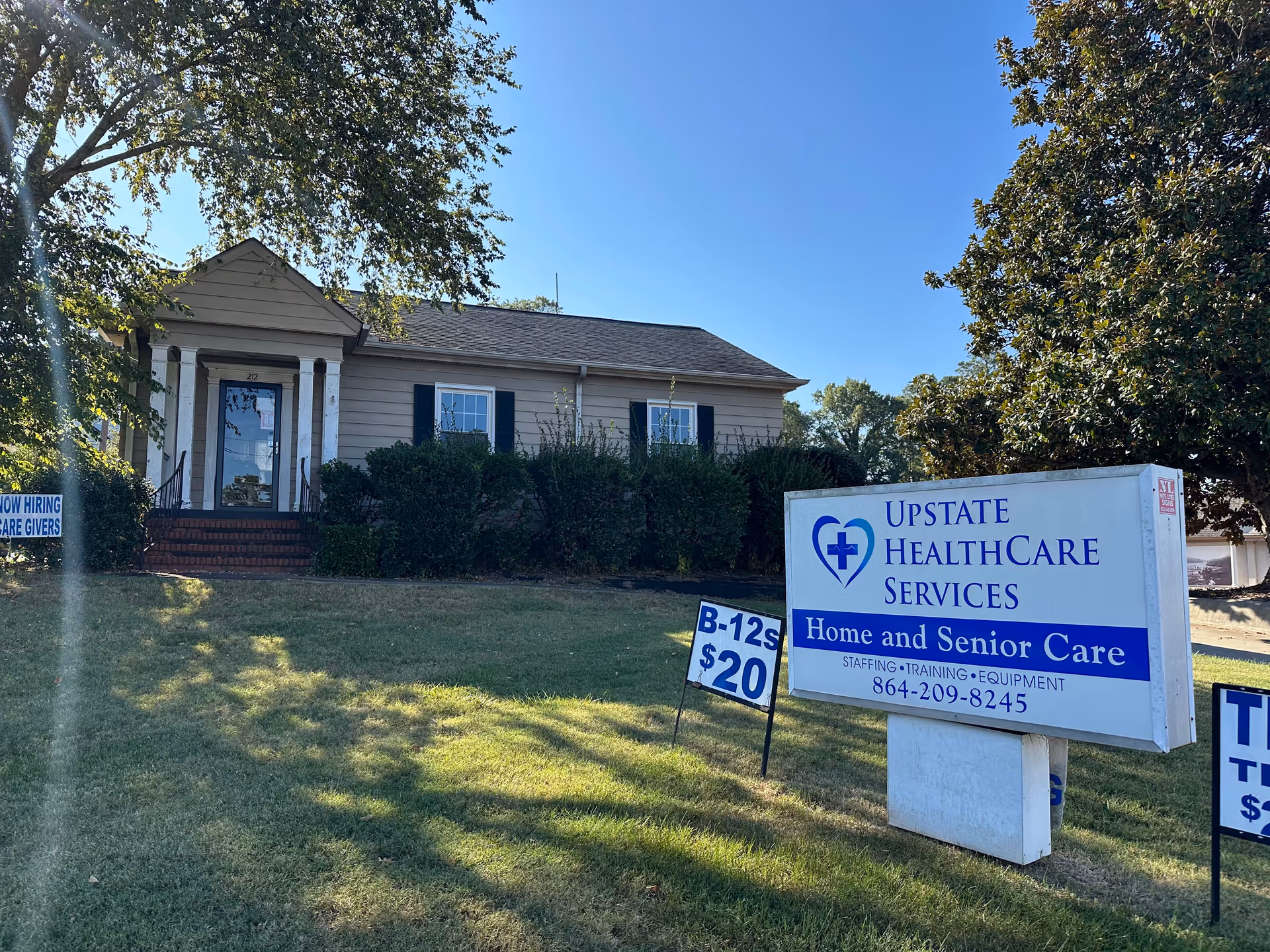 Single-story beige facility with front steps, shrubs, and a large Upstate HealthCare Services sign.