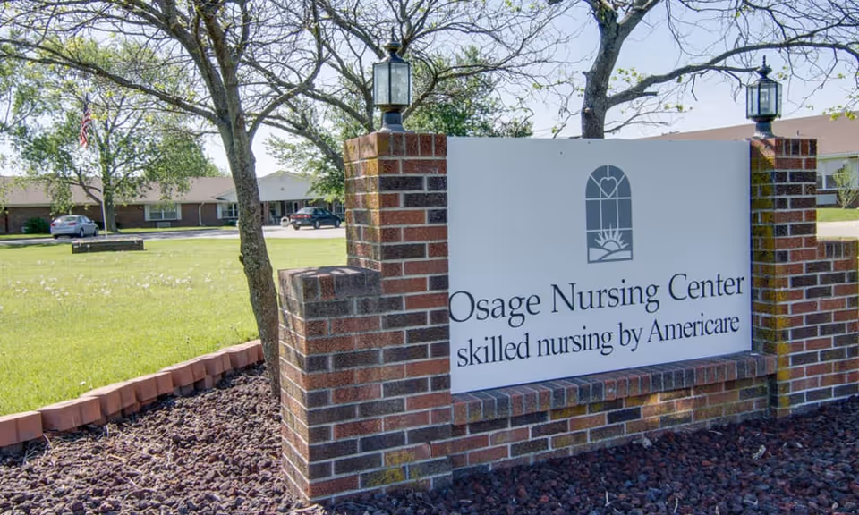 Brick entrance sign for Osage Nursing Center reading "skilled nursing by Americare" on a landscaped lawn in front of the facility.