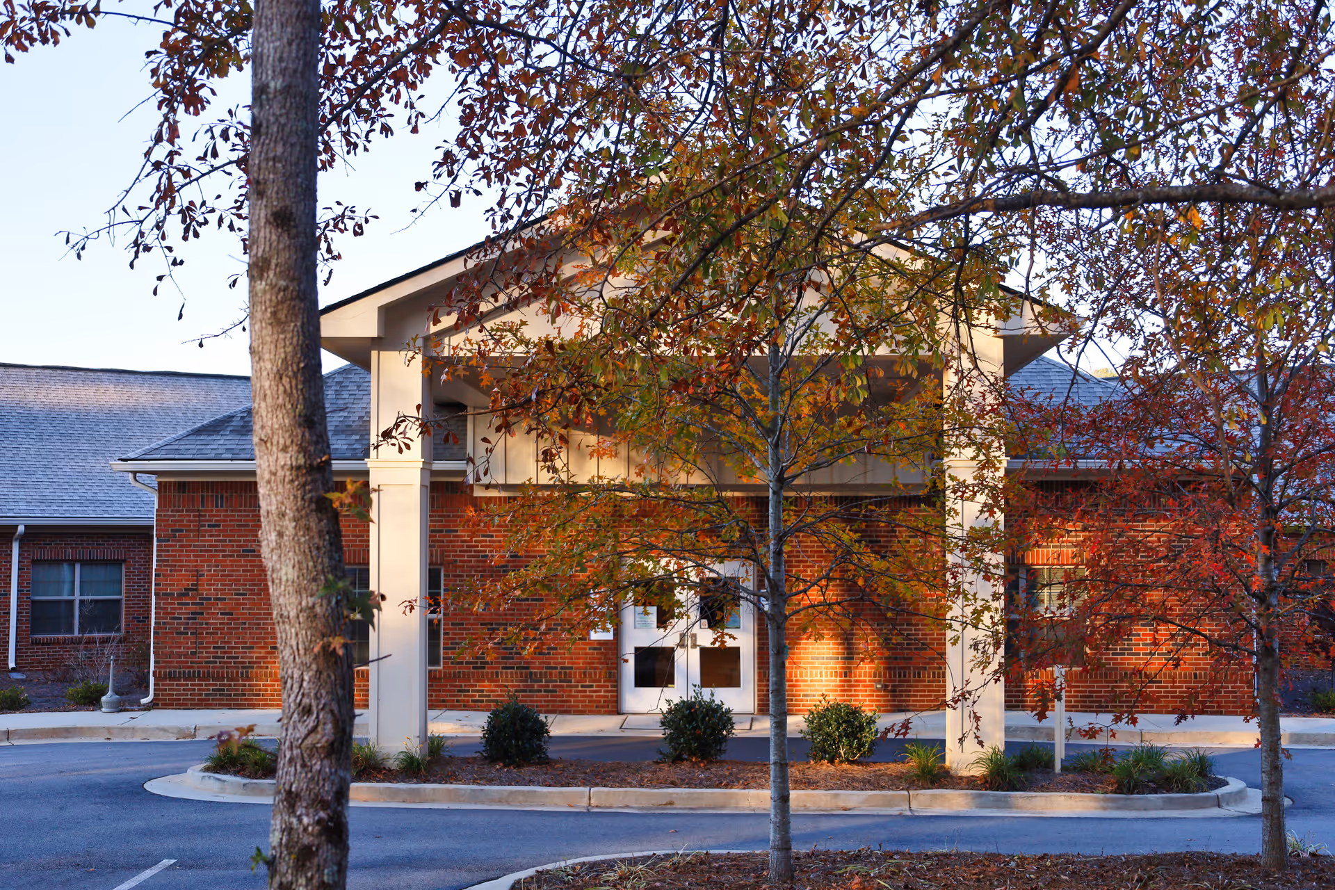 Exterior view of a brick hospice building with a covered entrance and trees.