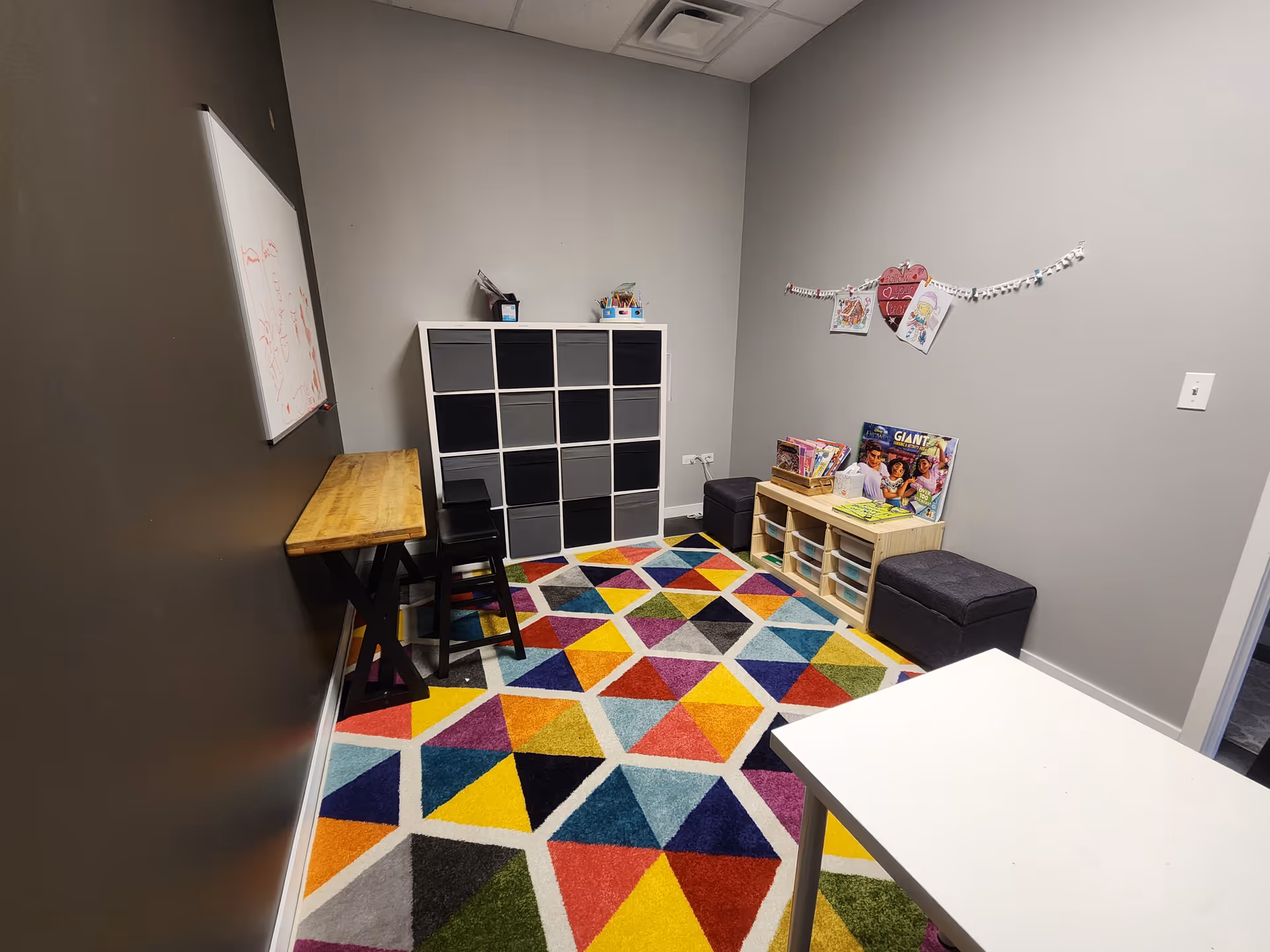 Small colorful activity room with cubby shelves, toys, and a whiteboard along gray walls.