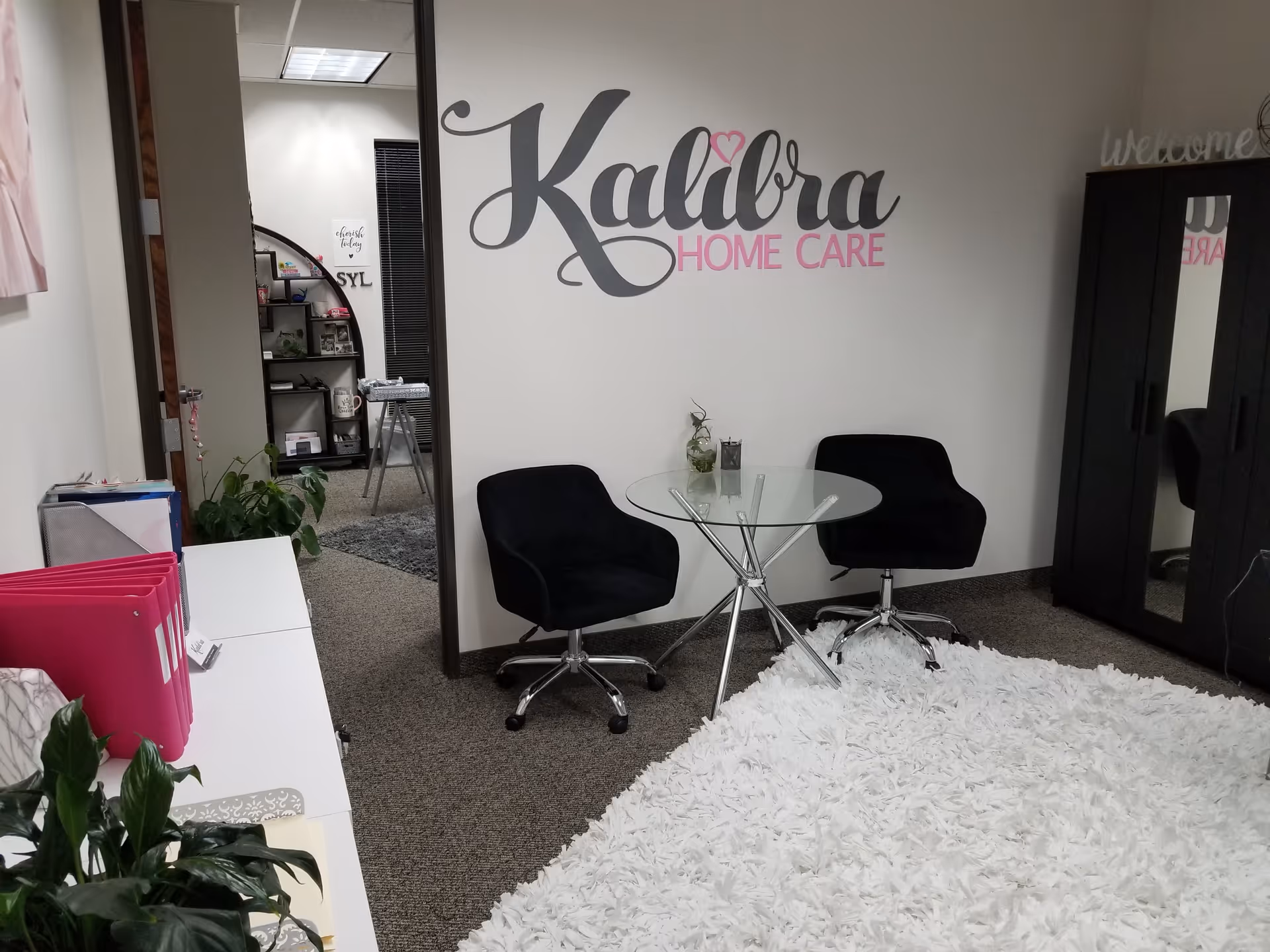 Reception area with round glass table, two black chairs, and Kalibra Home Care logo.