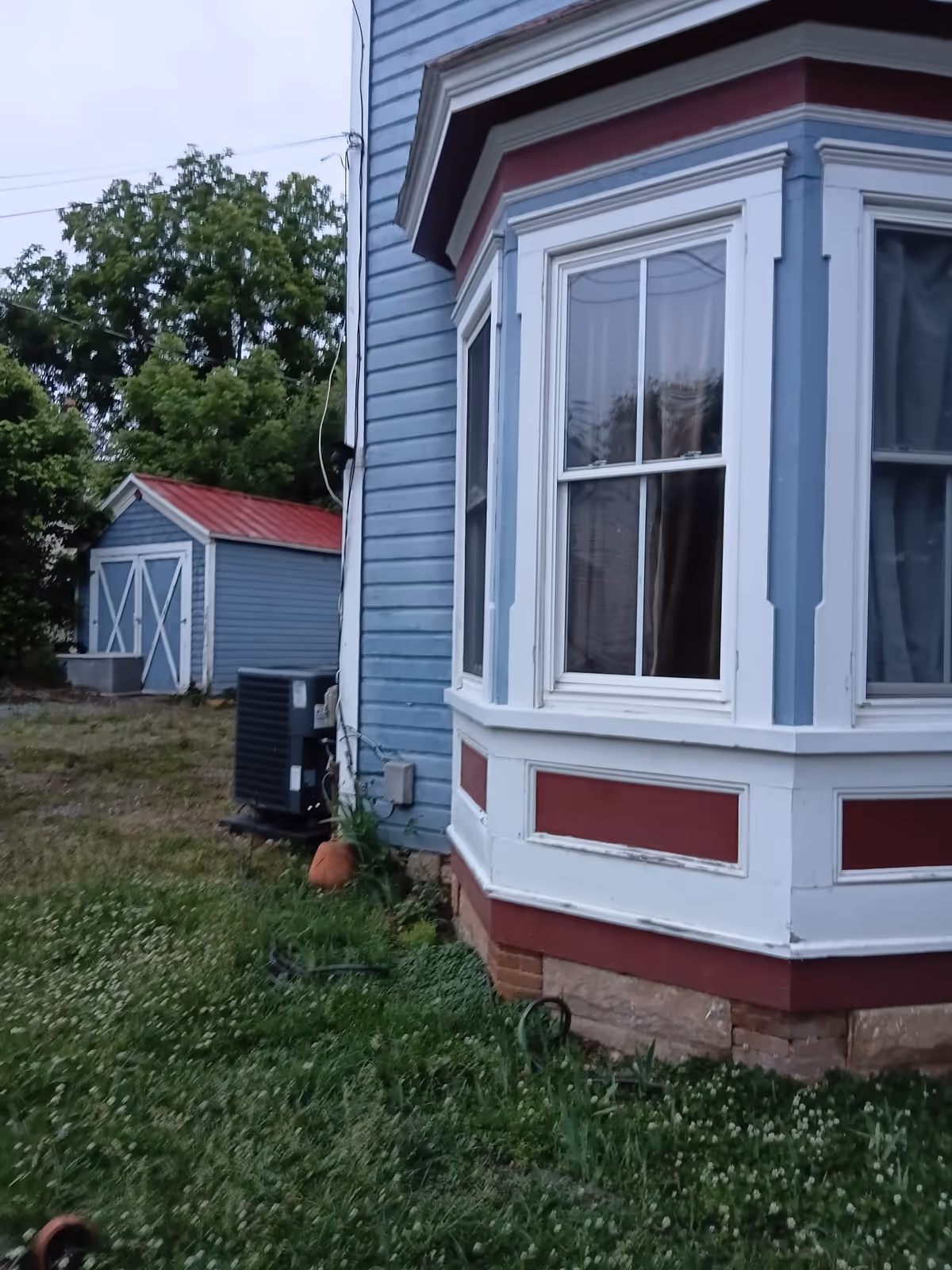 Blue exterior building with bay window, AC unit, and grassy yard nearby.