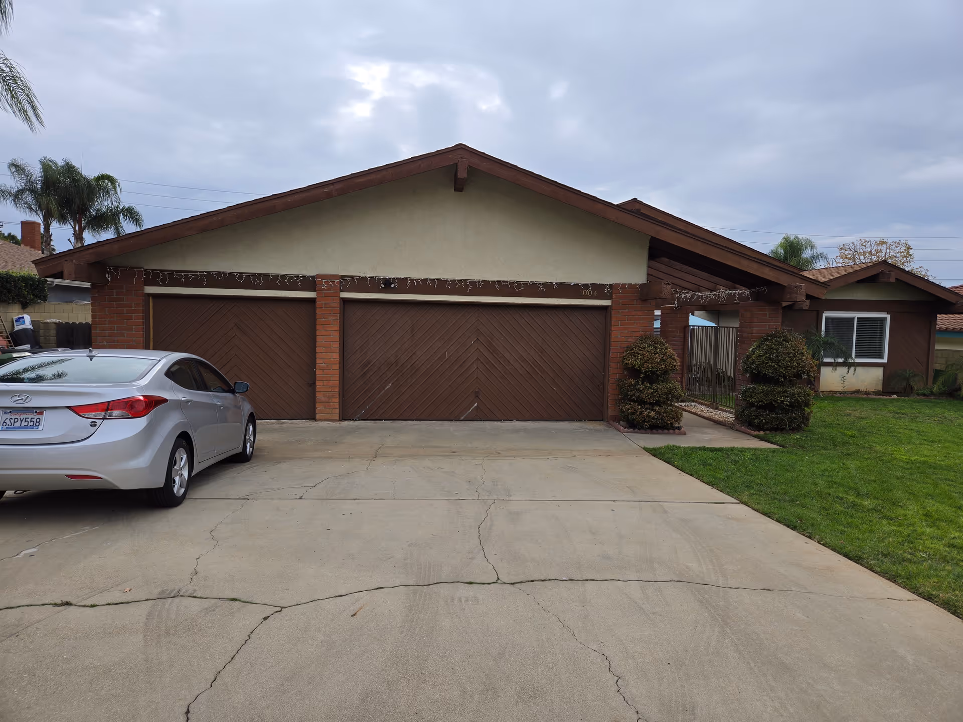 A single-story brick house with three-garage bays and a silver sedan in the driveway.