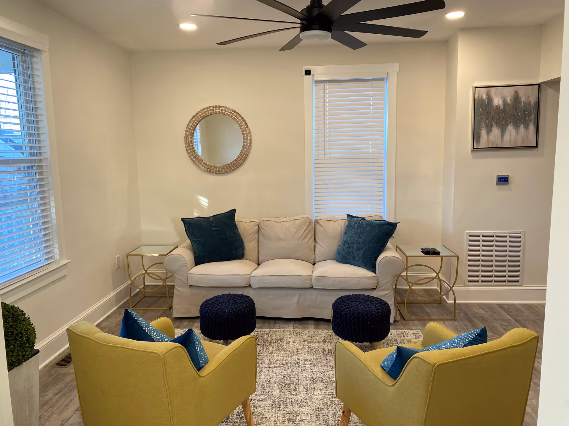Bright living room with a white sofa, yellow chairs, navy ottomans, and gold side tables.