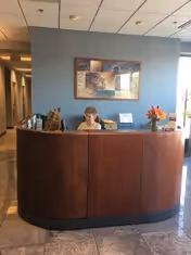 Curved wooden reception desk in a lobby with a staff member and blue wall.
