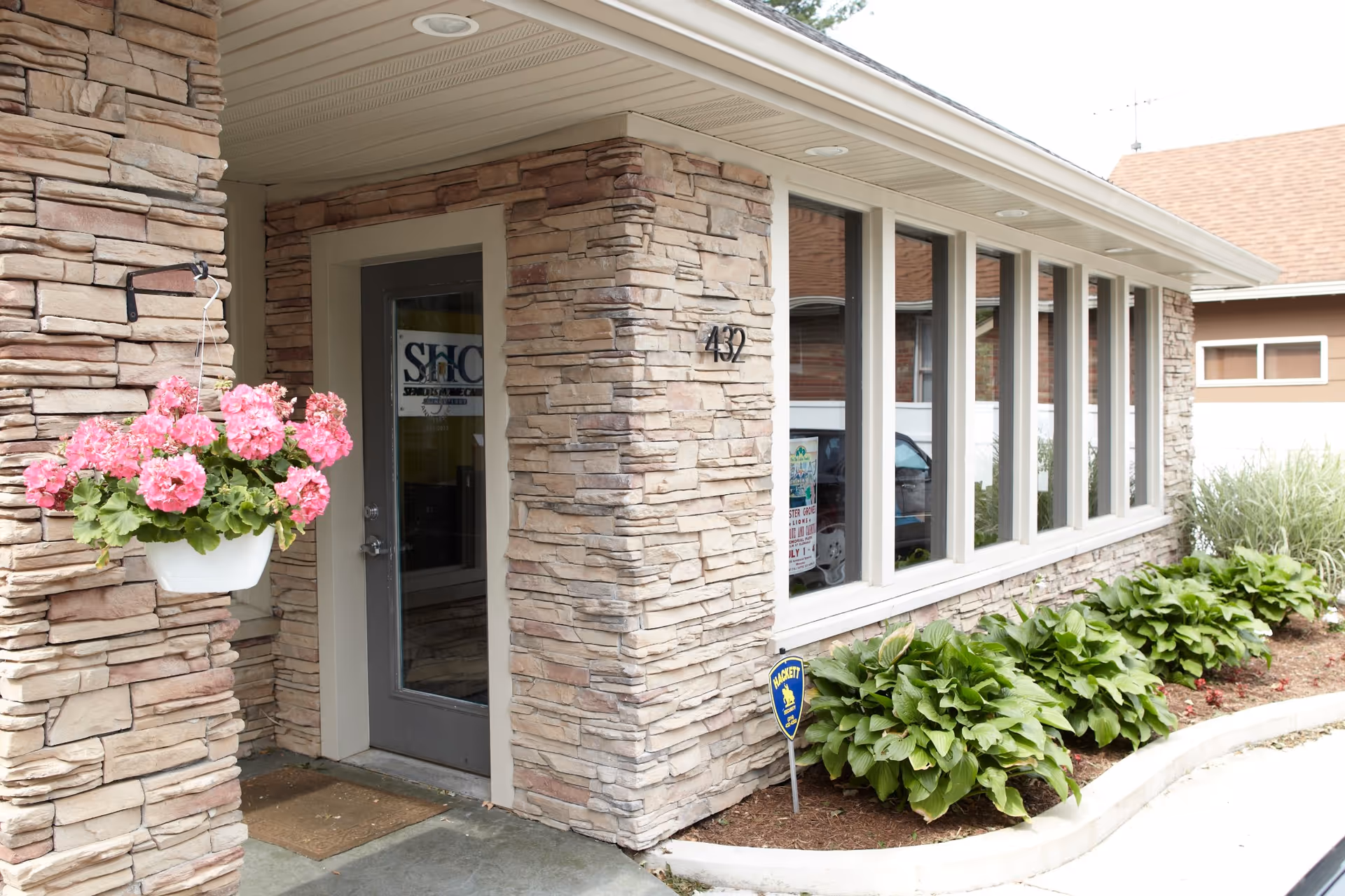 Stone-faced senior care building exterior with front entrance, windows, and hanging flowers.