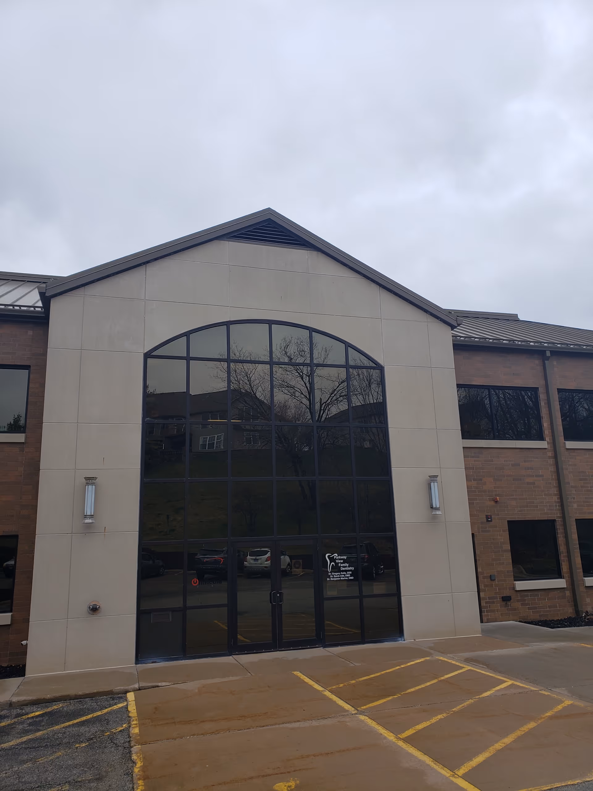 Front view of a modern healthcare facility with a tall arched glass entrance.