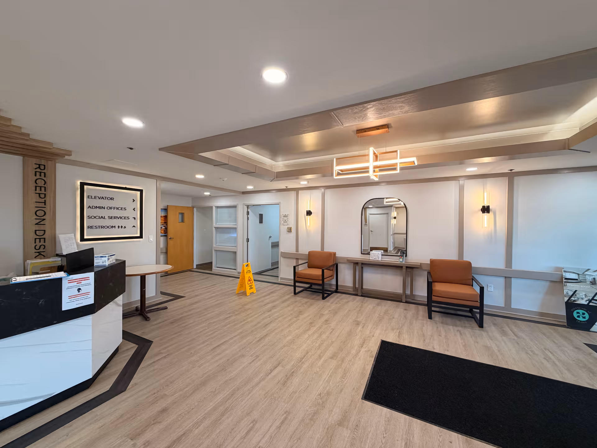 Bright senior living lobby with reception desk, seating, and a decorative mirror.