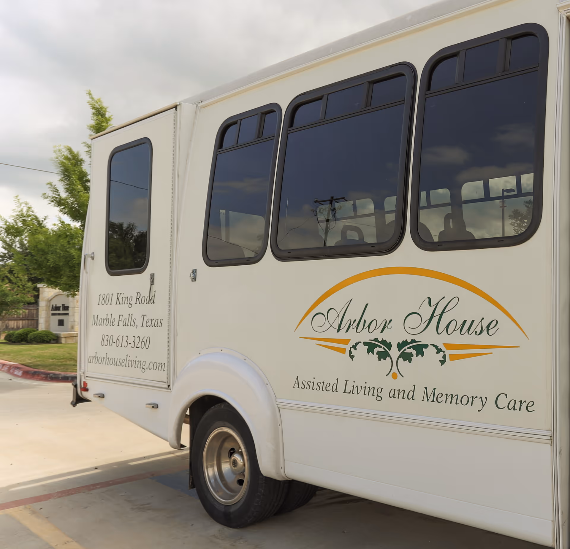 A white shuttle bus with Arbor House branding and the words Assisted Living and Memory Care parked in a driveway.