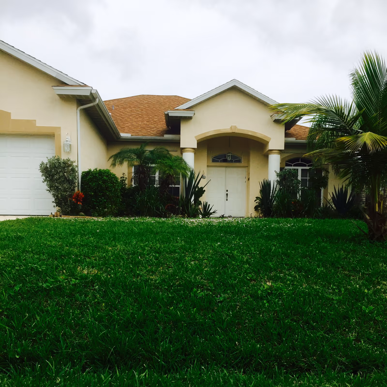 Front view of a beige single-story residence with a green lawn and palm plants.