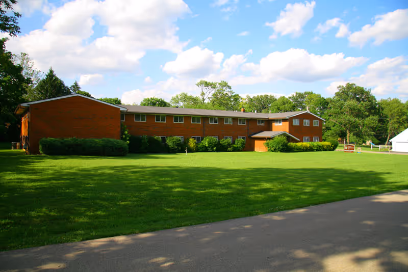Exterior view of a brick senior living facility with a large green lawn and trees.