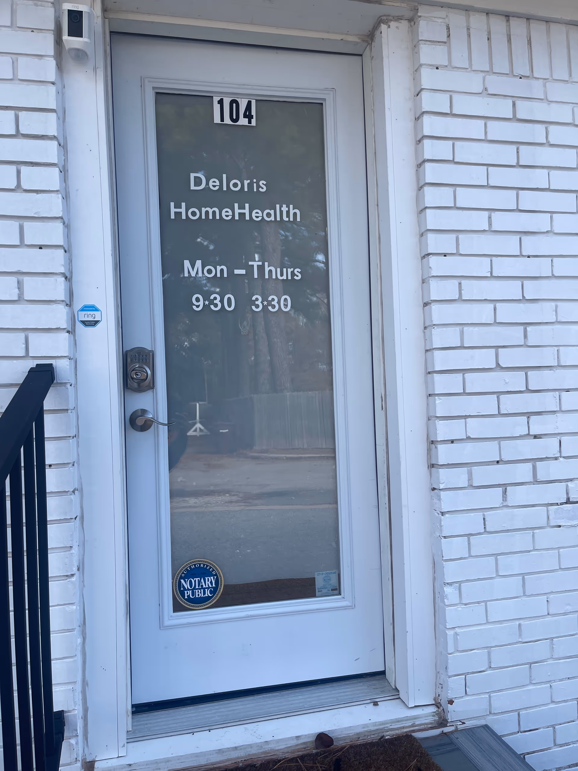 White brick exterior with glass door displaying Deloris HomeHealth, unit 104, and hours.