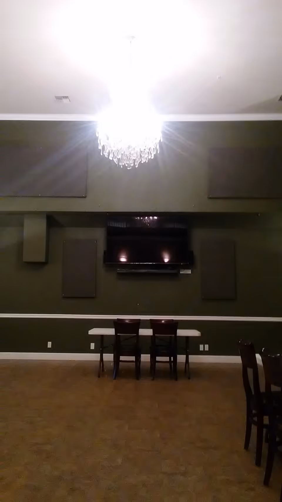 Dark green lounge area with chandelier, wall TV, and small table with two chairs
