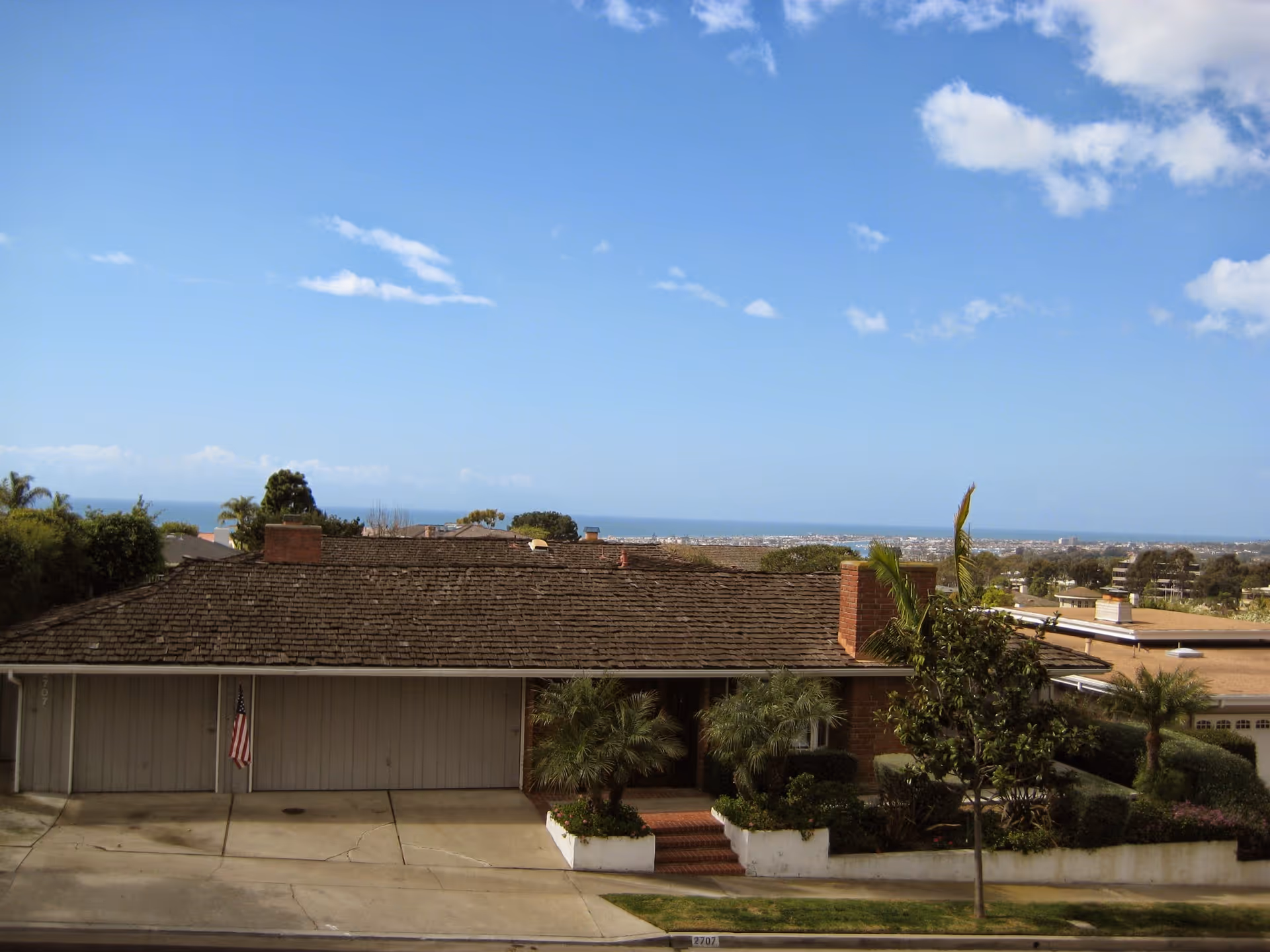 Front view of a single-story house with driveway and ocean horizon.