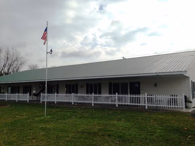 Single-story facility with white picket fence, flagpole, and a long front porch.