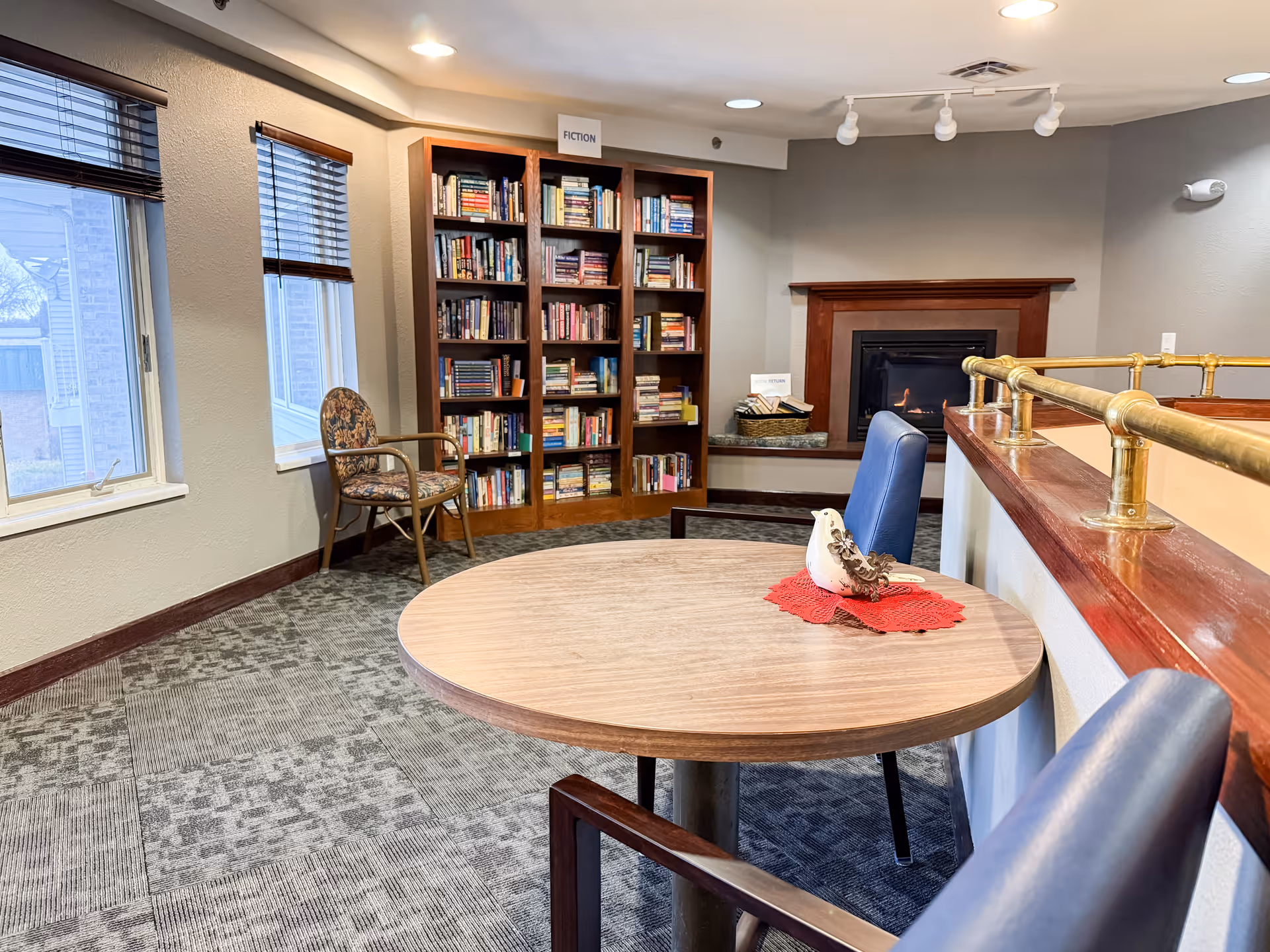 A cozy interior lounge with a round table, bookshelf, fireplace, and seating.