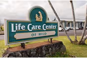 Front exterior of Life Care Center of Hilo with a green sign and palms