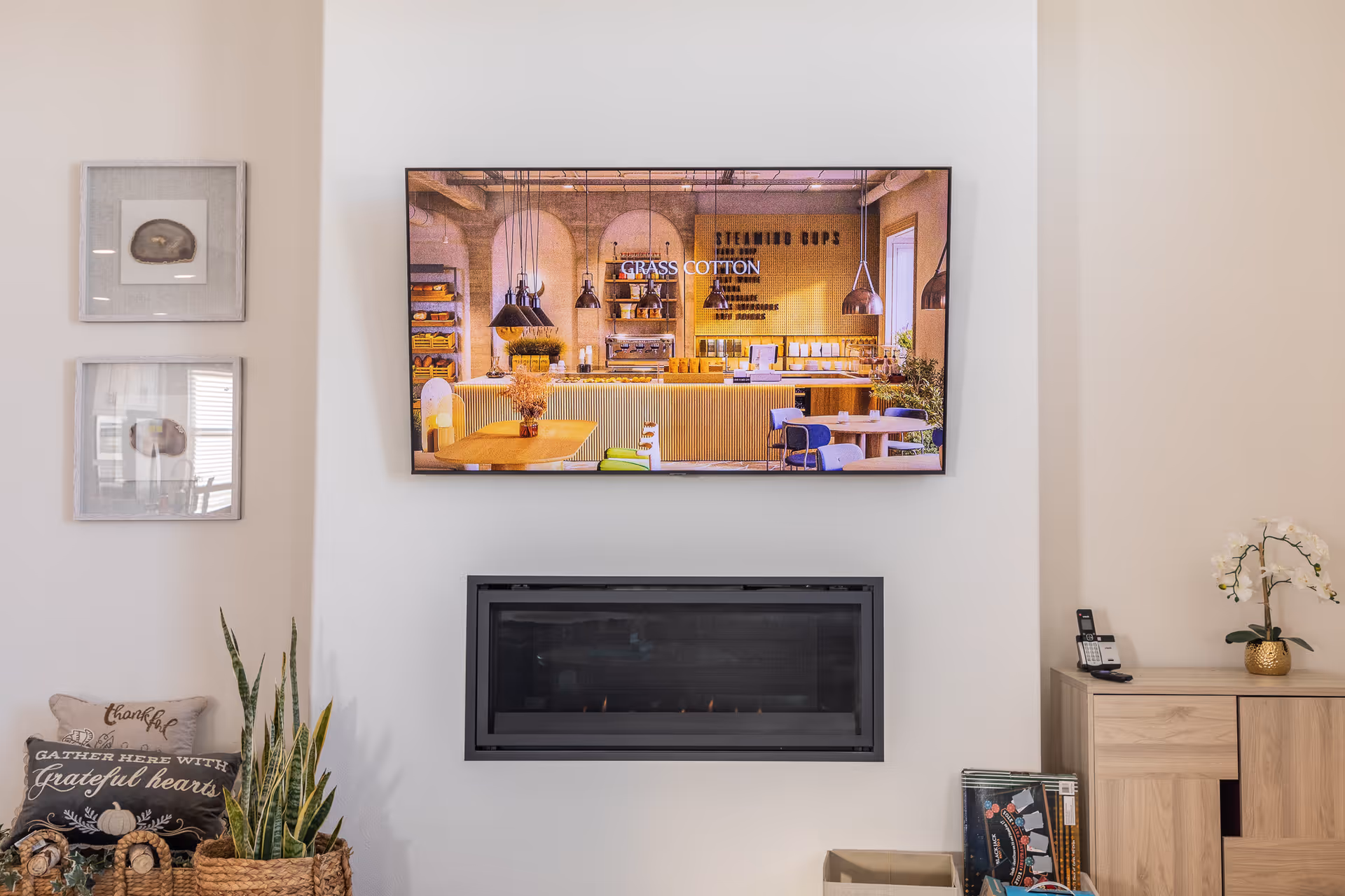 A living room area with a wall-mounted TV above a fireplace and decorative plants.