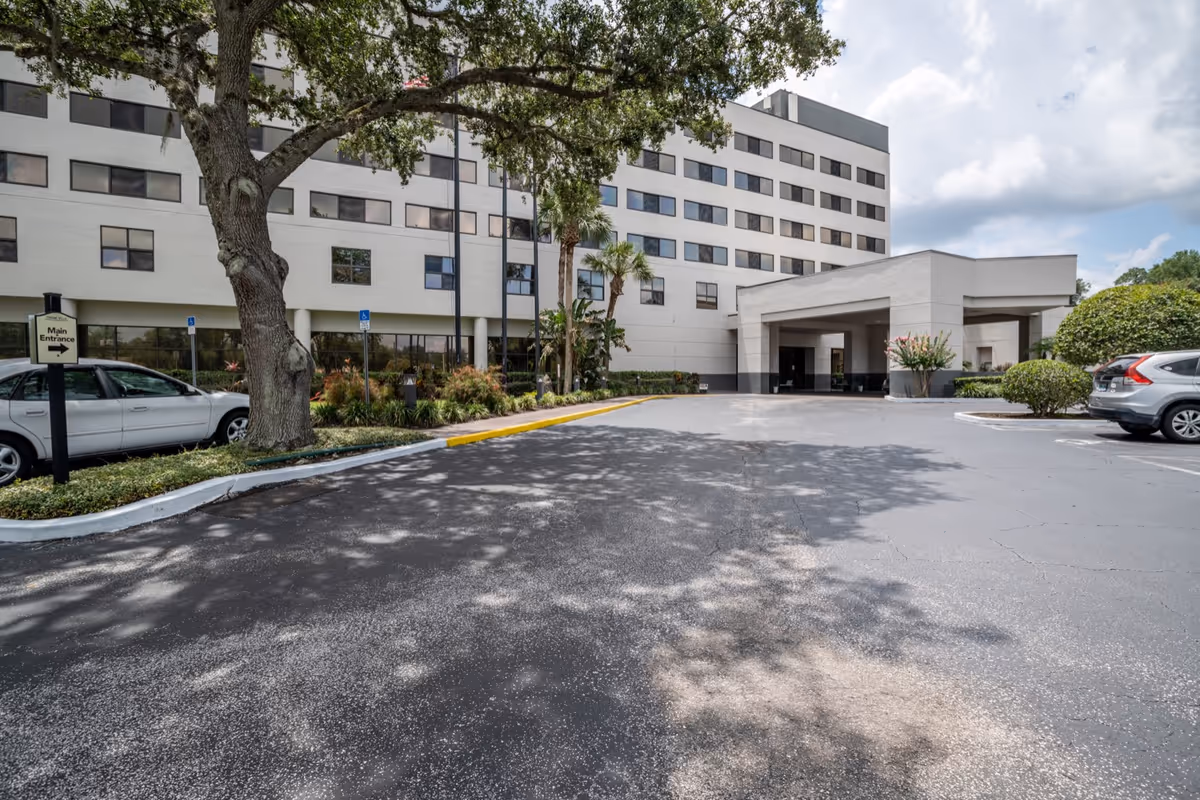 Exterior view of Grand Villa of DeLand with parking, trees, and a covered entrance.