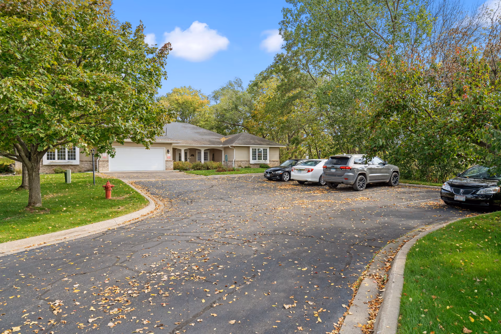 Front view of a single-story senior living facility with curved driveway and parked cars.