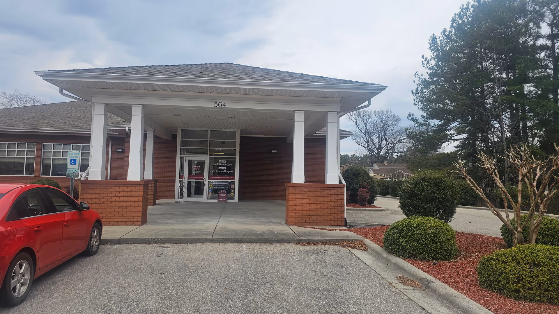 Brick hospice entrance with a covered drop-off area and surrounding landscaping.