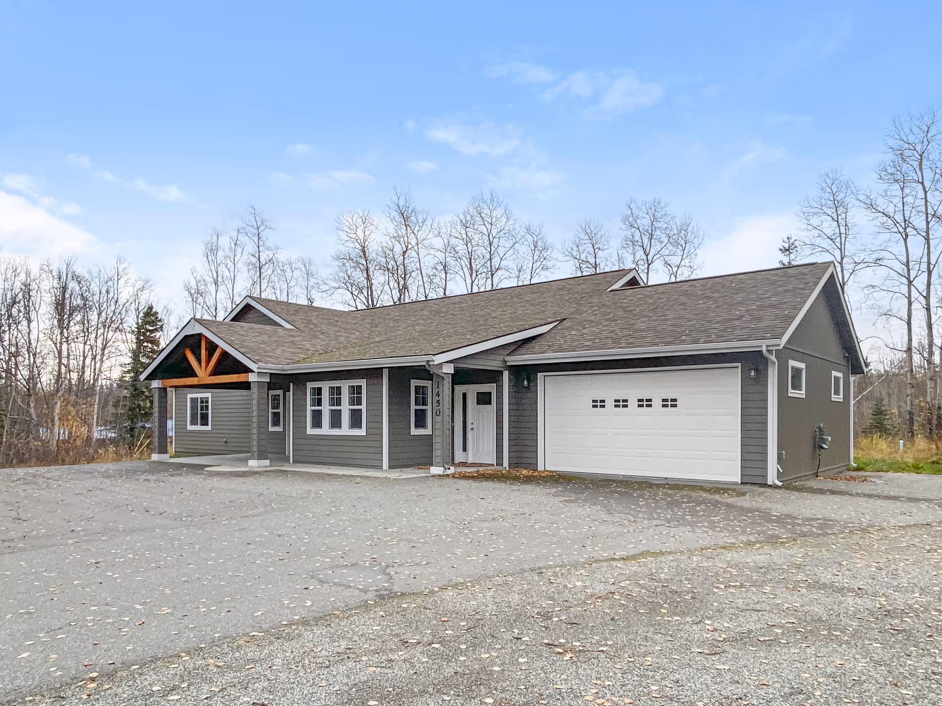 Gray single-story building shown from the front with a two-car garage and a leaf-covered lot.