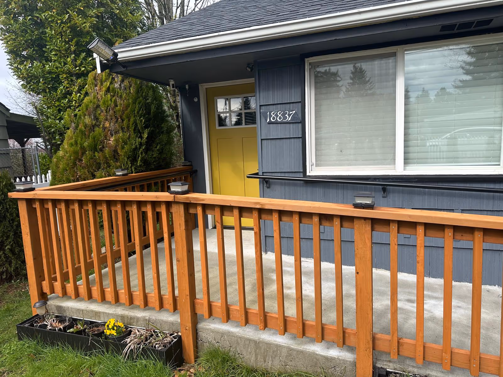 Blue exterior of a house with a bright yellow front door, wooden railing, and a window.