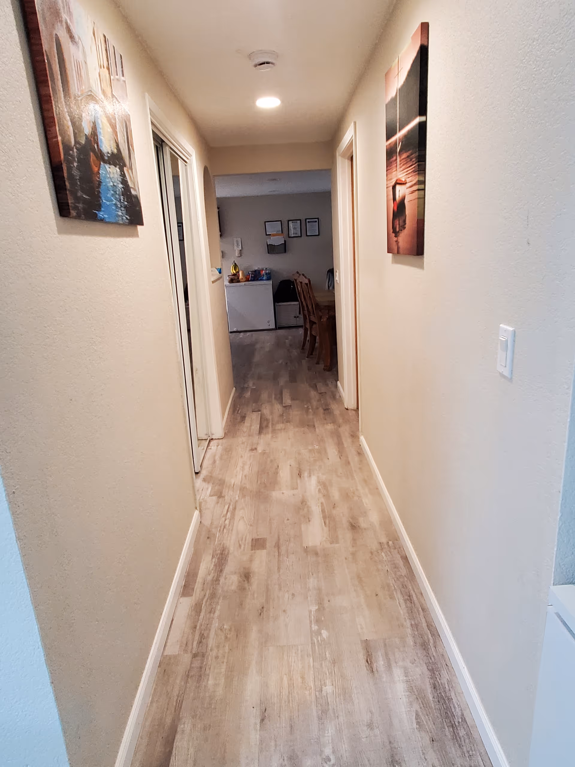 Narrow hallway of a senior home with wall art, leading to a dining area.