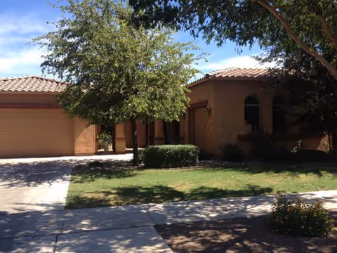 Front exterior of a brown stucco senior living building with a tree and lawn.
