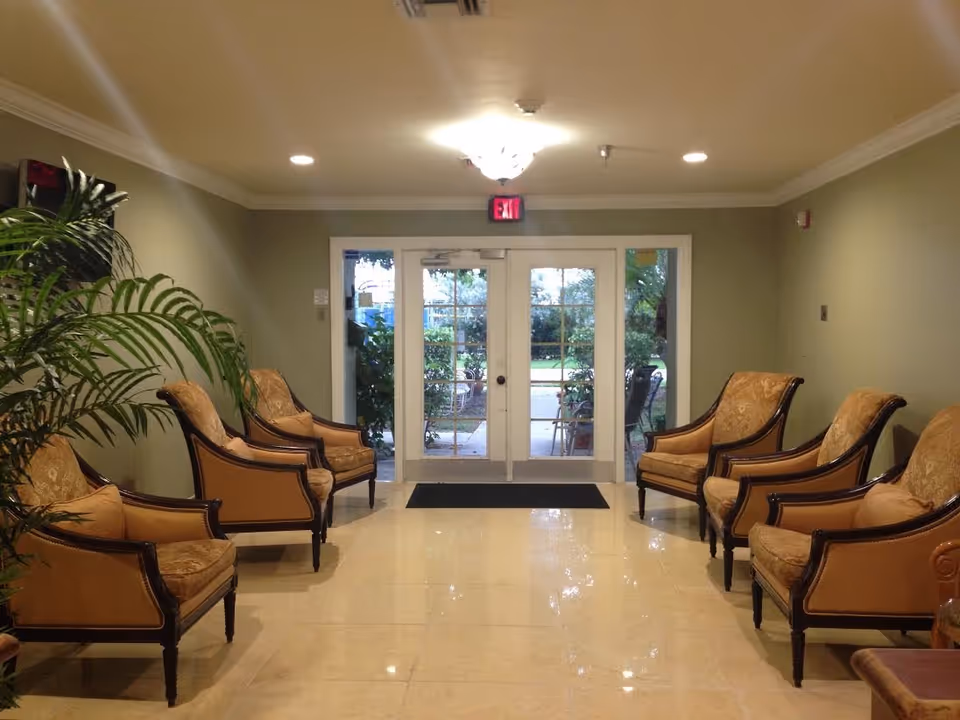 Lobby area of a senior living facility with symmetrical beige chairs facing glass doors and plants.