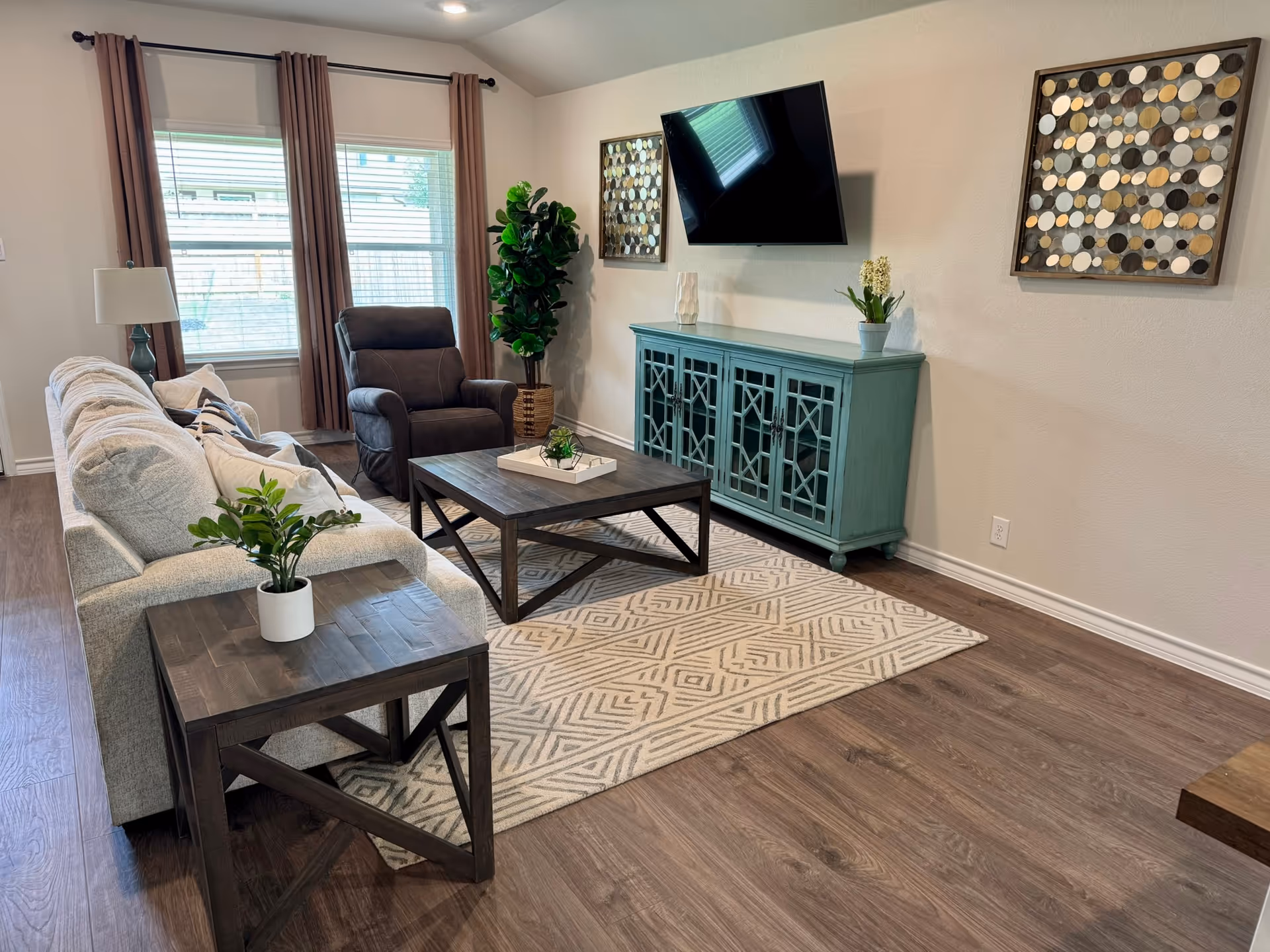 Cozy living room with sofa, recliner, TV, teal cabinet, plants, and patterned rug.