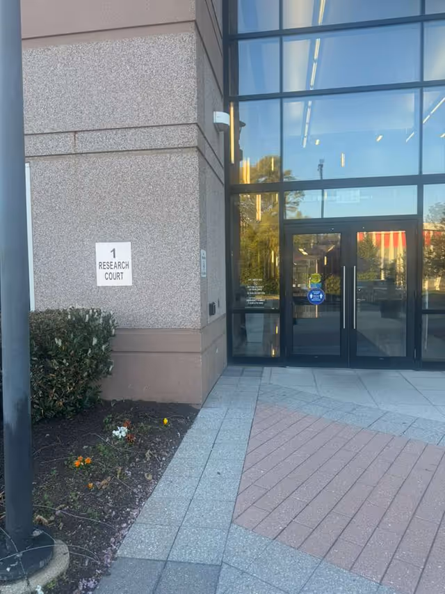 Exterior entrance to Ambition HomeCare building with glass doors and a Research Court sign.