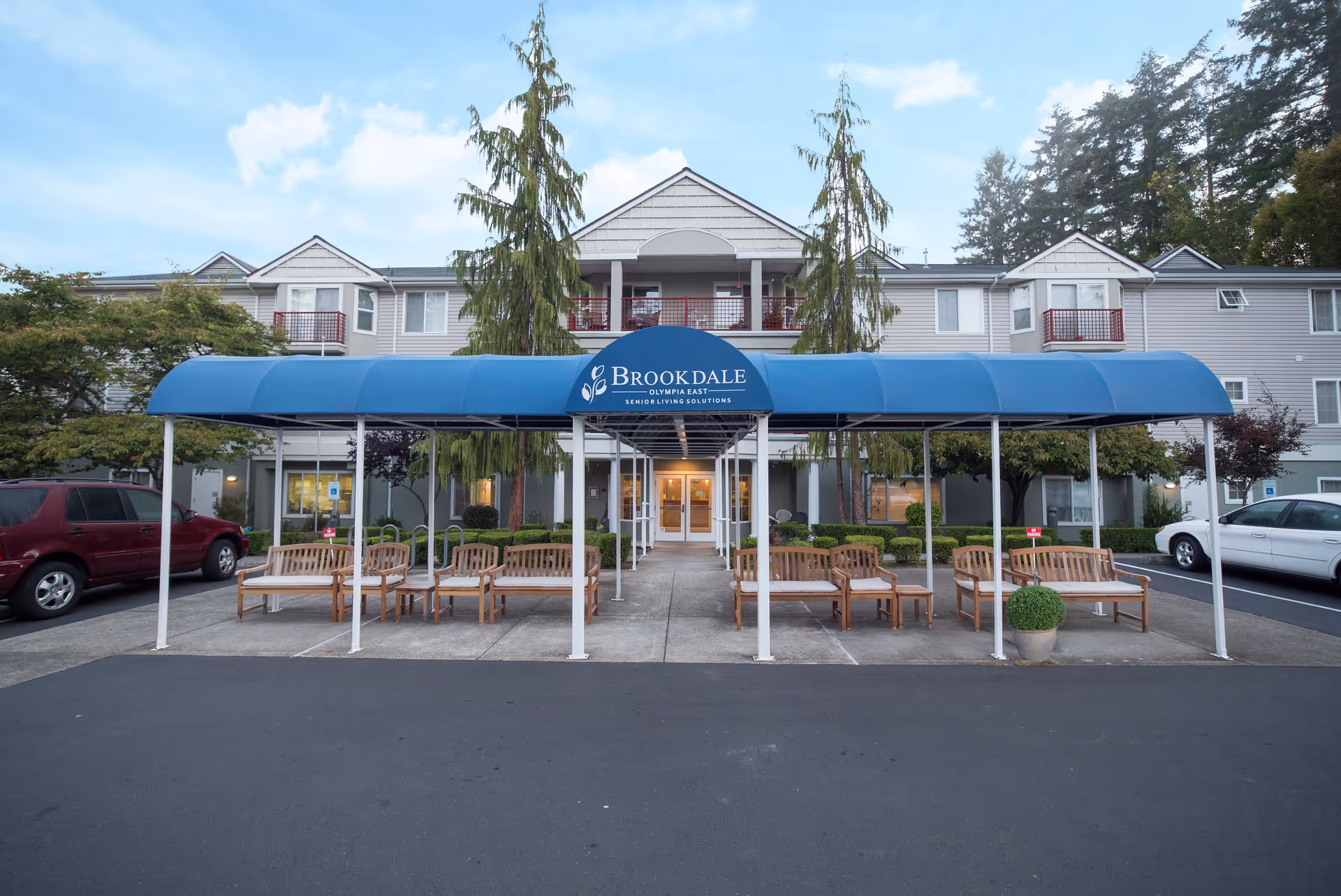 Front of Brookdale Olympia East senior living facility with a blue canopy and benches.