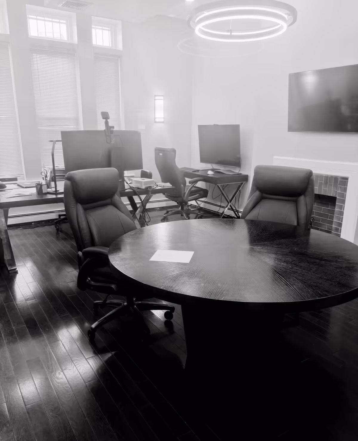 A modern conference room with a circular table, leather chairs, computers, and a wall-mounted TV.