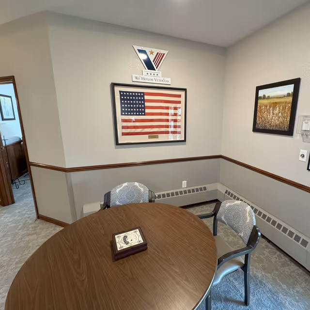 Round wooden dining table with patterned chairs in a small interior room displaying American flag artwork.
