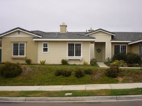 Single-story beige senior living building with front entrance, windows, and landscaped lawn.