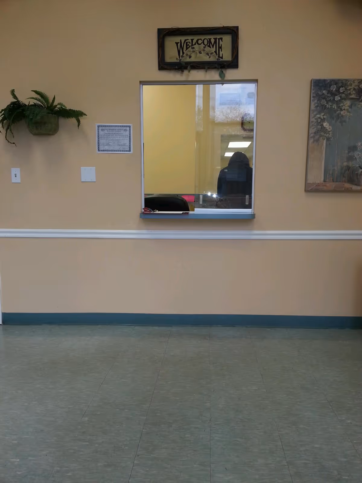 Beige hallway interior with a small window service counter and a decorative Welcome sign.