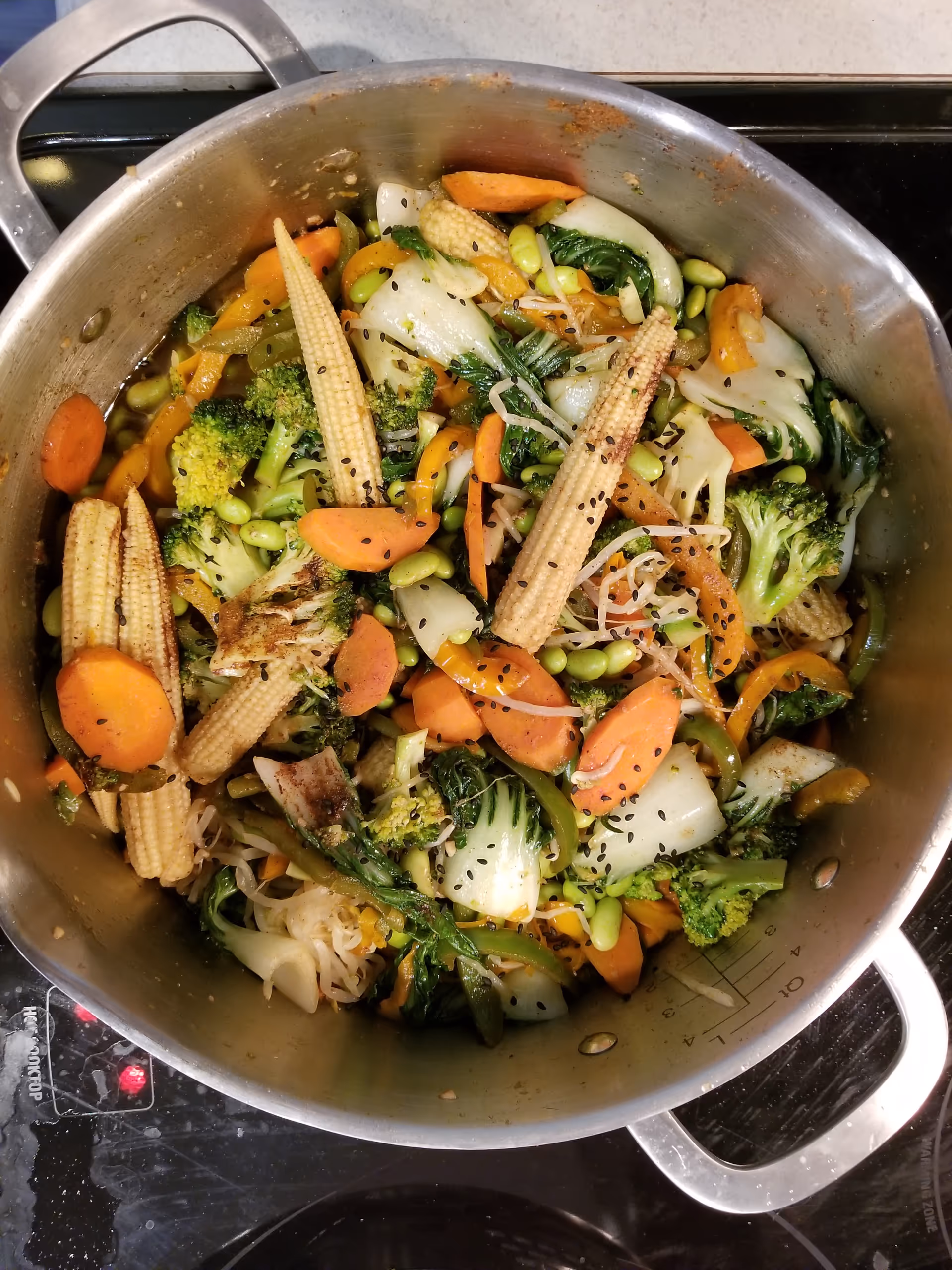 Stainless pot on stove filled with colorful mixed vegetables for cooking.