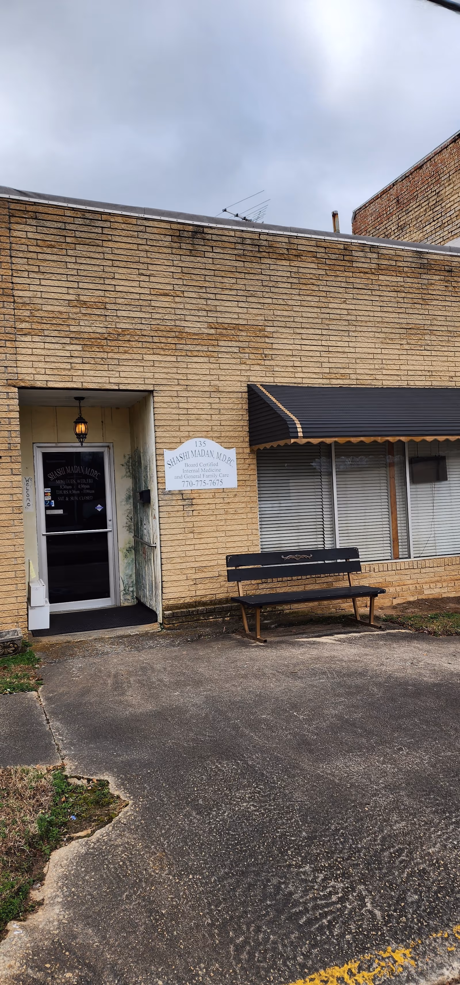 Brick building exterior of a facility with front entrance, sign, and a bench beneath an awning.