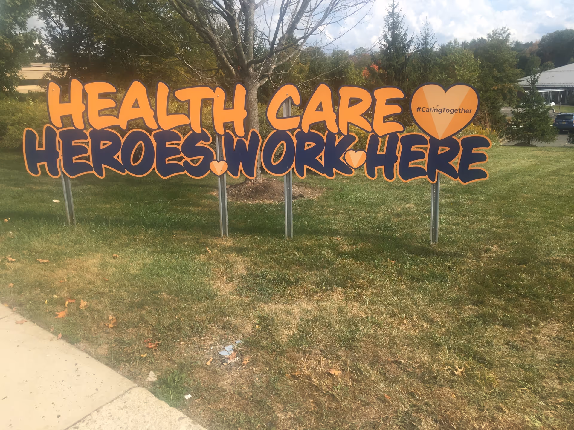 A large orange sign on a grassy lawn says Health Care Heroes Work Here