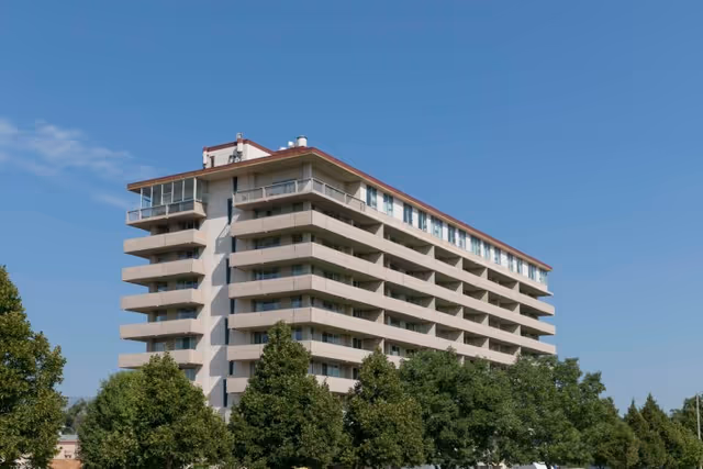 Multi-story beige residential/medical building with stacked balconies and trees in front under a clear blue sky.